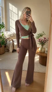 Uma mulher vestindo a blusa marrom canelada transpassada e a calça flare combinando, em pé em uma sala ensolarada, imagem gerada a partir de uma foto de produto em estilo flat lay.