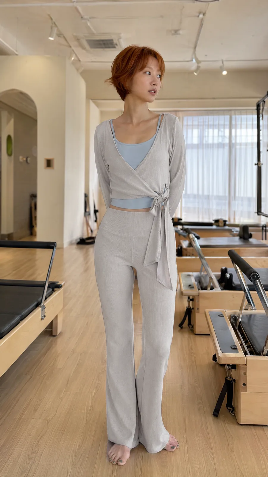 Frau in grauem, geripptem Wickel-Set steht in einem Pilates-Studio