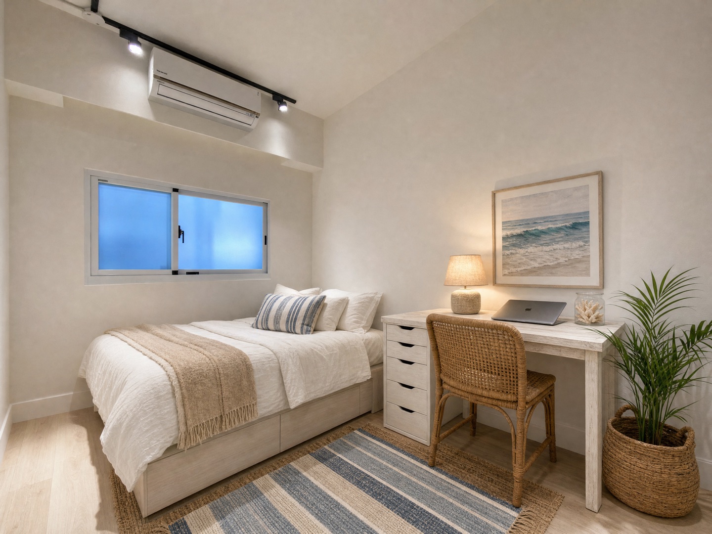 The same bedroom in Coastal style: white bedding with a striped cushion and a beige throw, striped rug over jute, rattan chair, a seascape print above the desk, table lamp and a potted palm; window, air conditioner and track light unchanged